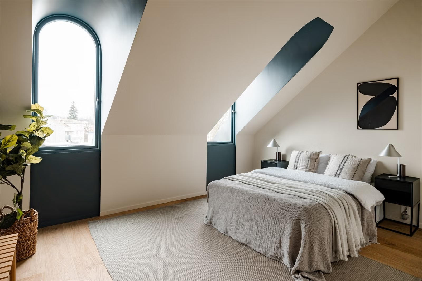 Attic bedroom with arched windows and sloped ceiling in the Living Under the Sky apartment in Oslo by IK-architects
